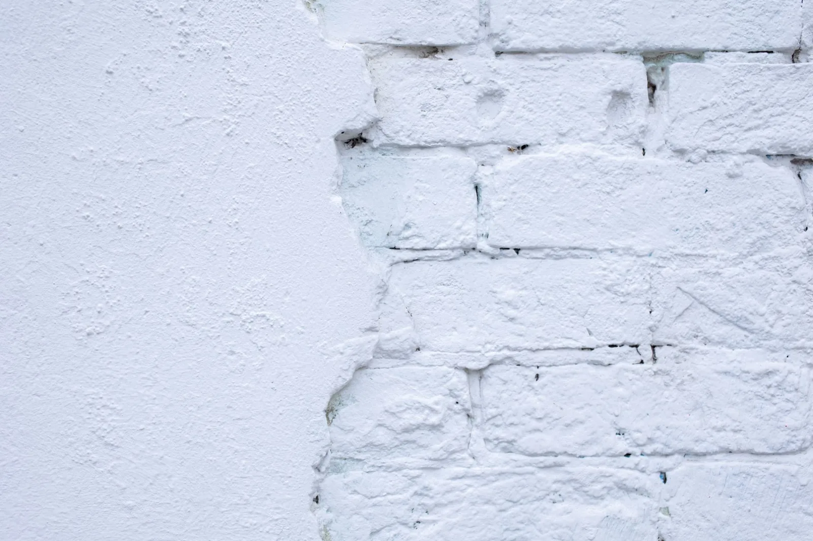 Textured background of white wall with uneven brick surface and wavy line of plaster edge
