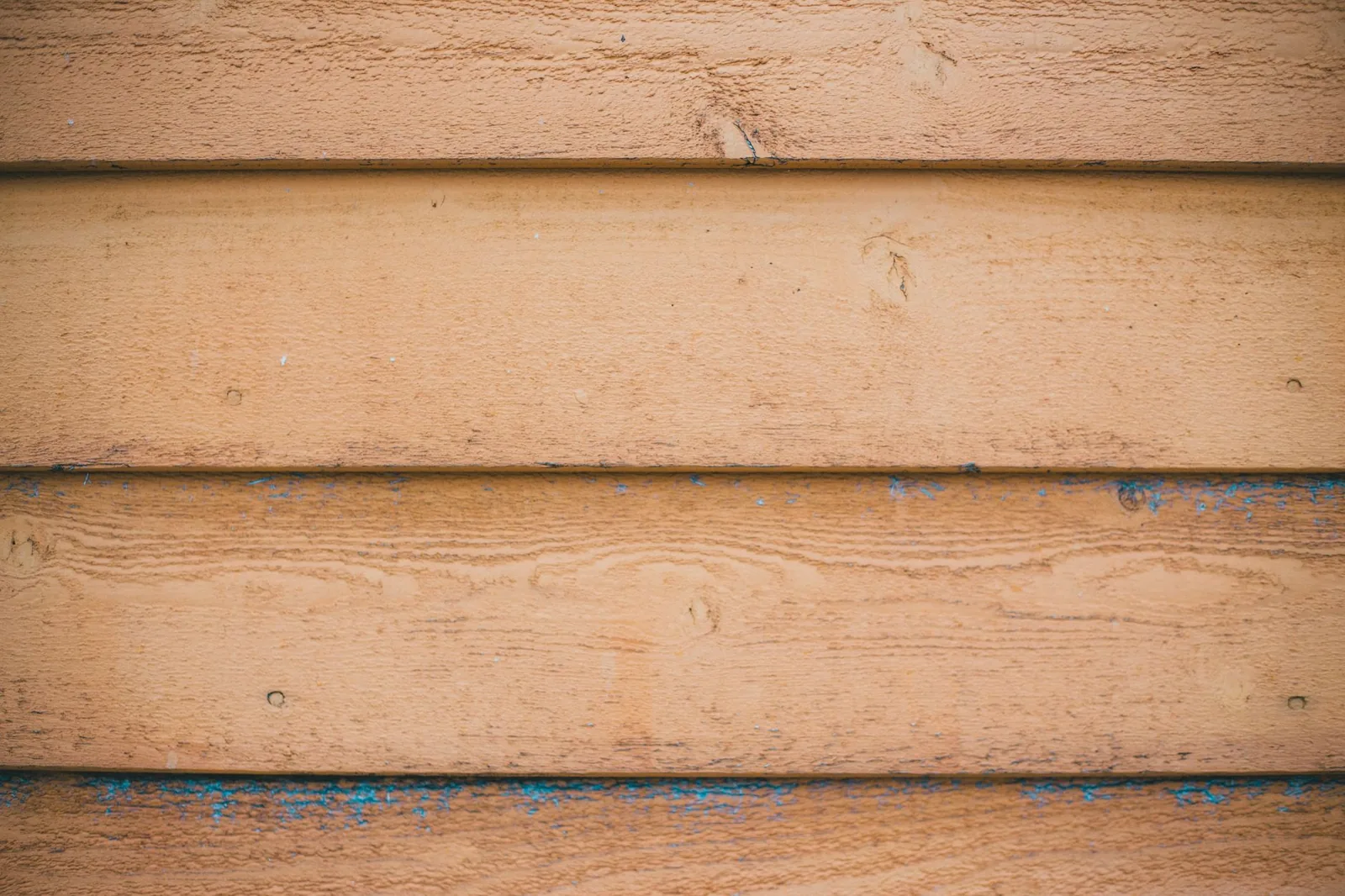 Shabby beige-painted wood planks showing the weathering and upkeep real wood siding demands
