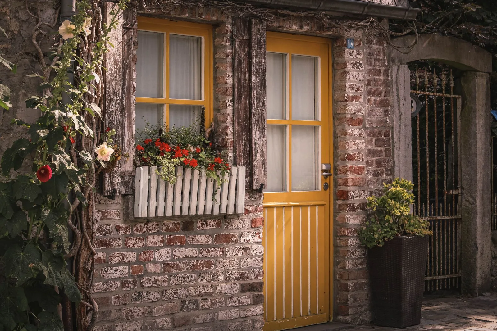 Rustic brick entryway with a yellow wooden door and vibrant flower arrangements — a warm curb appeal trend for 2026