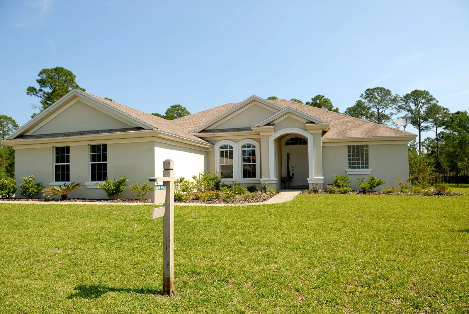 A charming suburban house with a lush lawn and a for sale sign under a clear sky